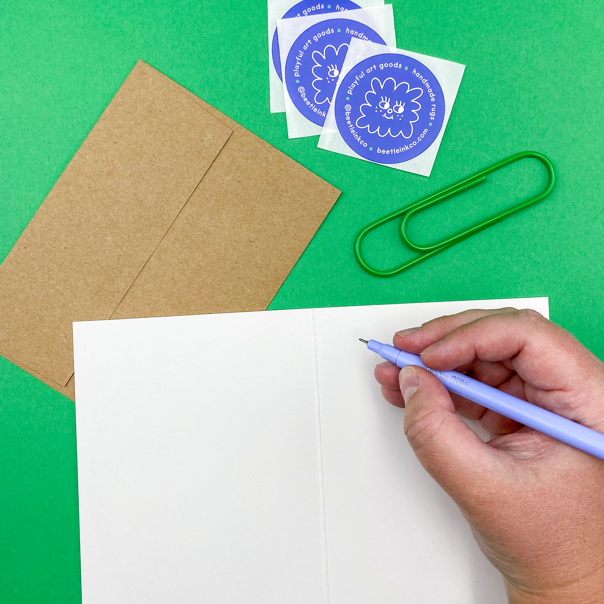 The artist is writing in an open risograph printed greeting card at her art desk. 