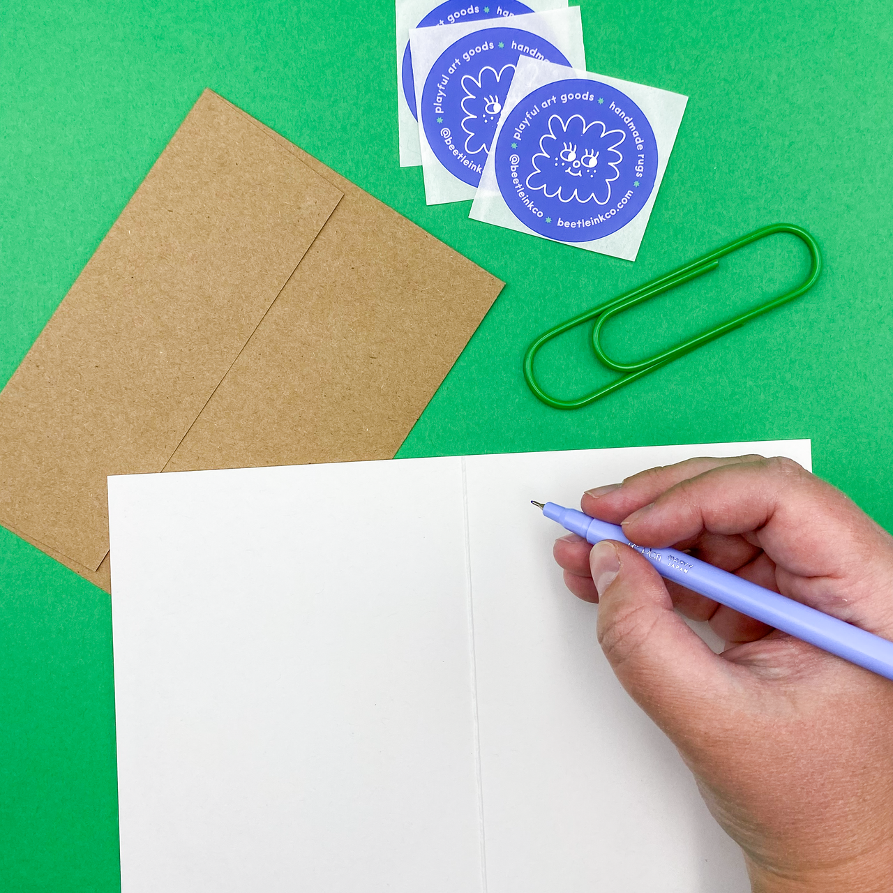 A risograph printed greeting card with kraft envelope, sits on a periwinkle background.